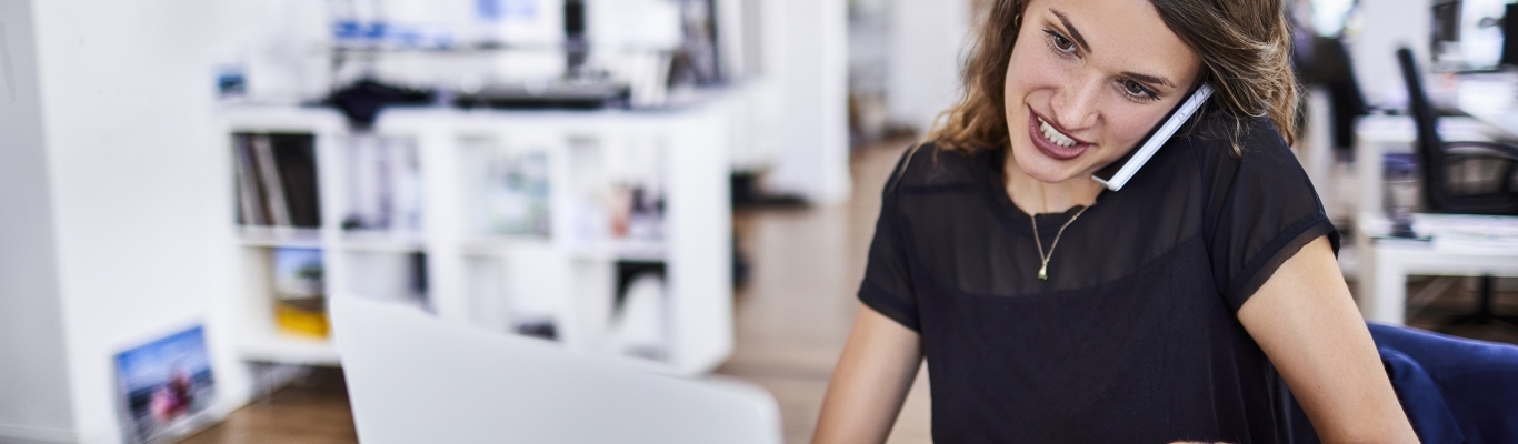 Woman on cell phone and working on laptop in office